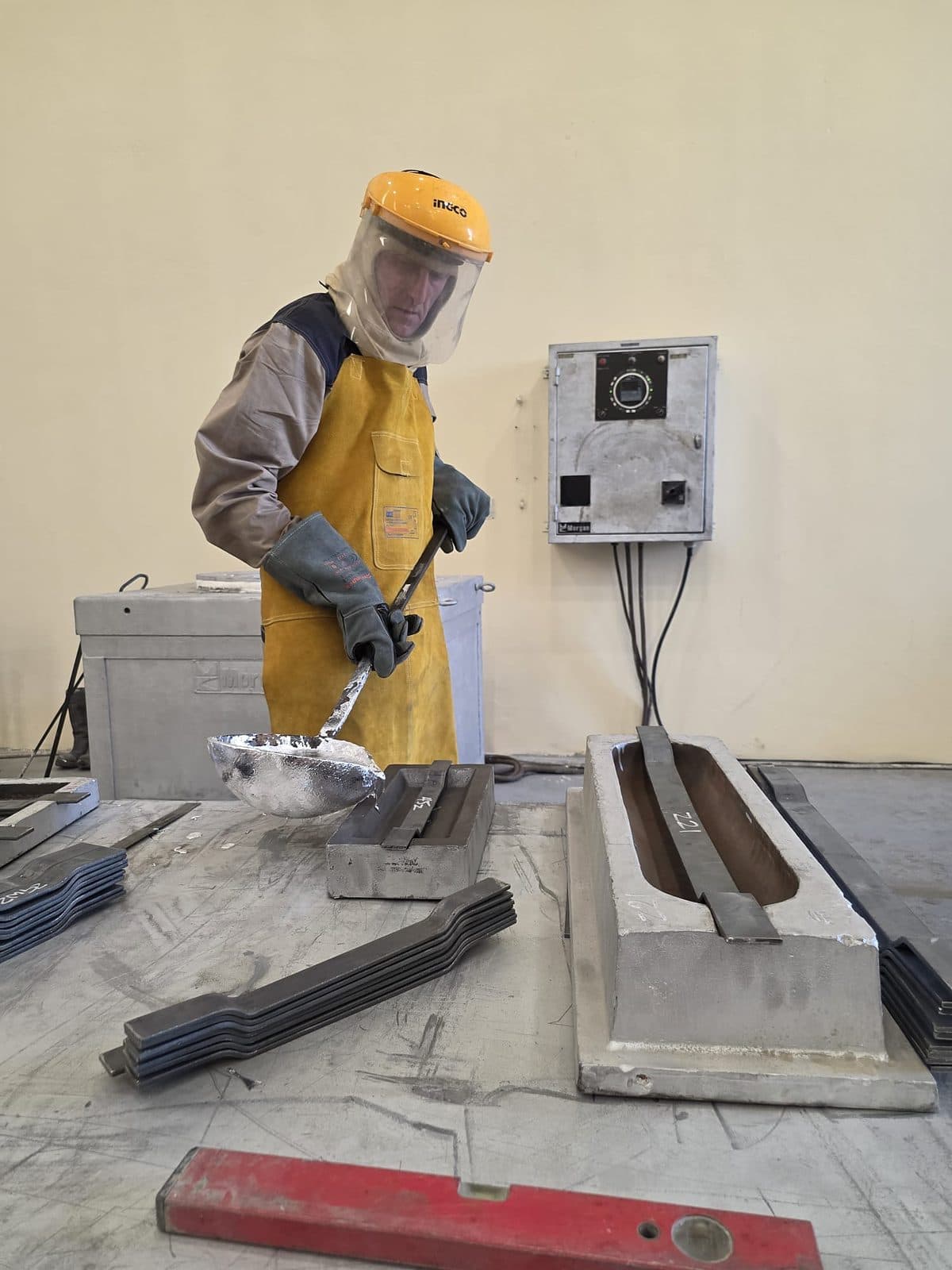 Operator in full foundry PPE pouring molten alloy